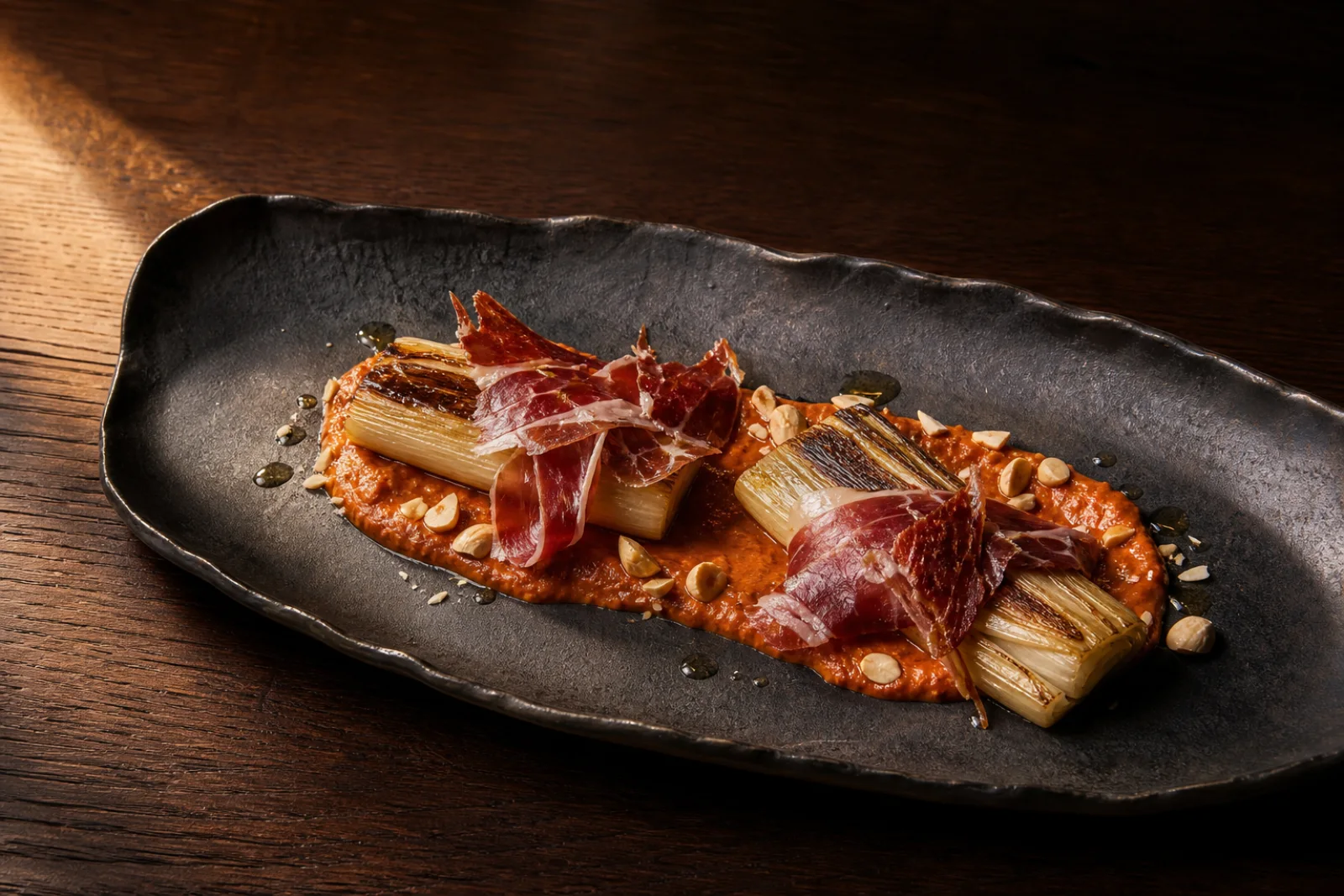 Puerros confitados con salsa romesco de almendras y jamón serrano